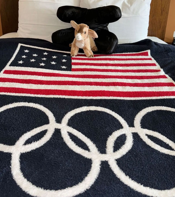 CozyChic Team USA Flag Olympic Ring Throw on a bed with pillows and a stuffed animal. 