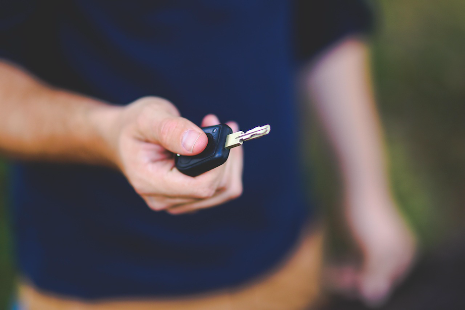 A close-up of a person holding out car keys, symbolizing the opening of the insurance "risk window" the moment a stranger starts a test drive in a private car sale.