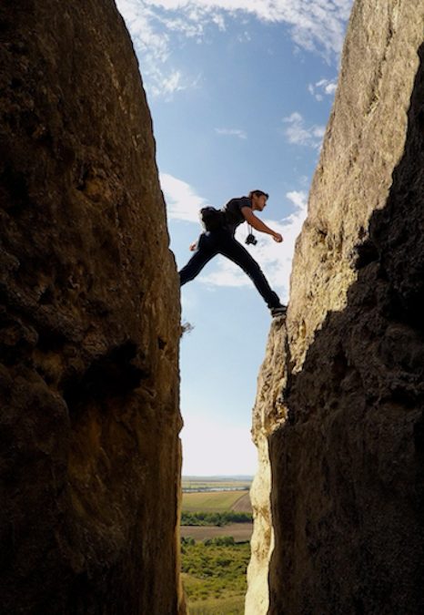 A man crossing a gap between two rock formations, illustrating the Trade Me and insurance payout gap that Quashed helps Kiwis understand and avoid in 2026.