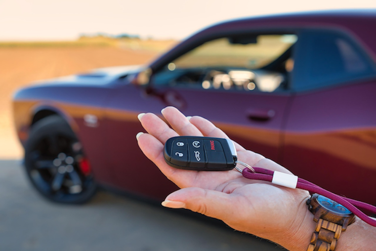 A hand holding a car key fob in front of a vehicle, representing the "handover grey zone" between payment and the formal change of ownership notification to NZTA.