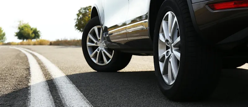 A close-up view of a car's wheels and chassis parked on a paved road with white lane markings, illustrating vehicle maintenance and safety standards for New Zealand drivers in 2026, explained by Quashed.