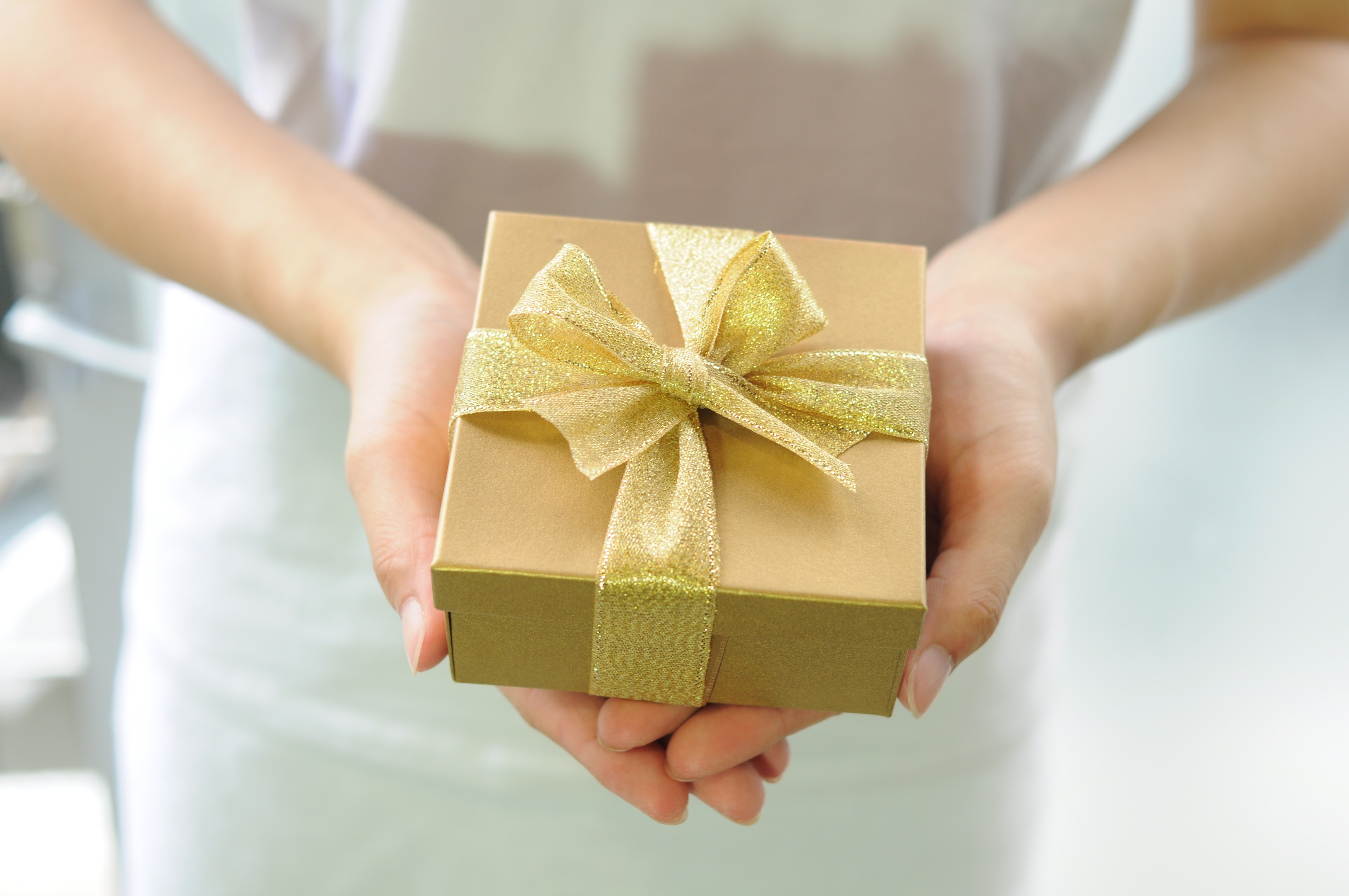 A woman holding a gift wrapped in golden wrapping paper and tied with a golden bow.
