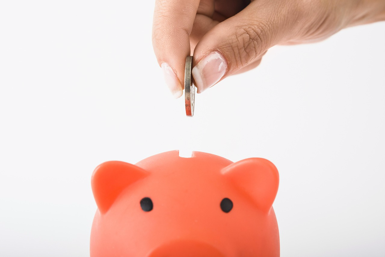 A hand placing a coin into a piggy bank, representing the potential for Kiwi drivers to save on car insurance premiums to offset the high national average petrol price in 2026.