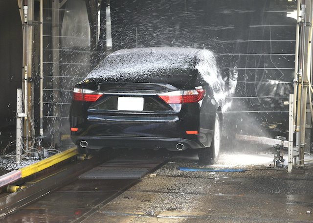 A car passing through a touchless car wash in New Zealand, showing a safer alternative to brush-based automatic washes.