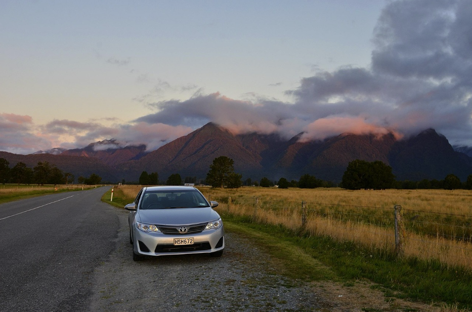 Silver Toyota parked beside a quiet New Zealand road at sunset, with mountains and clouds in the background — representing reliable car insurance protection and peace of mind for Kiwi drivers