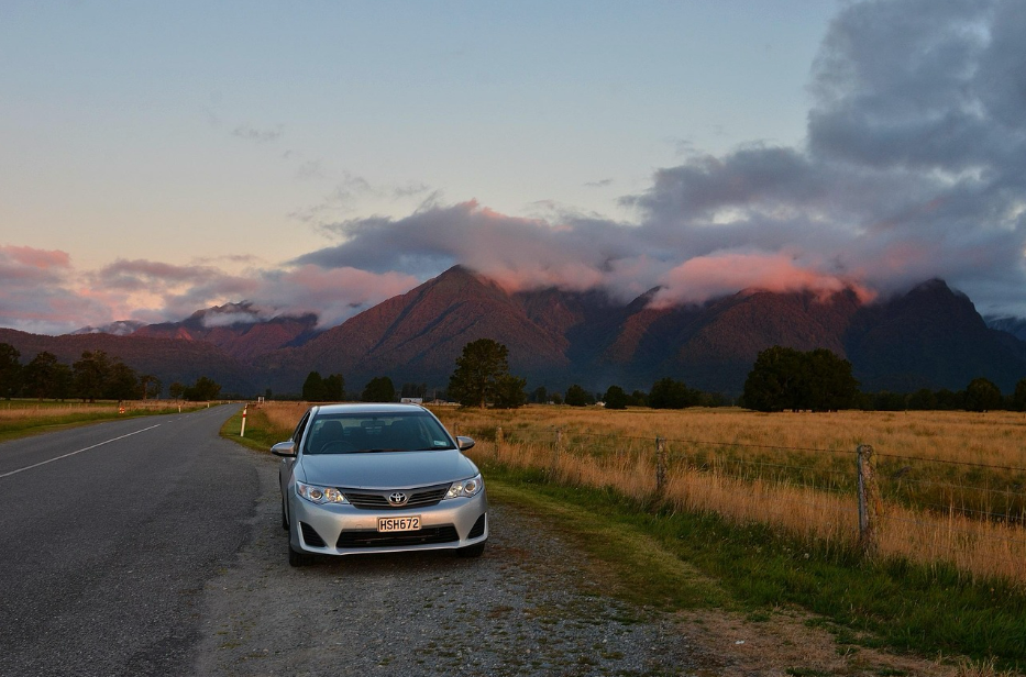 Silver Toyota parked beside a quiet New Zealand road at sunset, with mountains and clouds in the background — representing reliable car insurance protection and peace of mind for Kiwi drivers