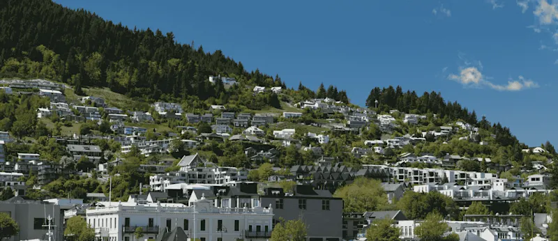 Neighboring New Zealand houses featured in a Quashed 2026 insurance guide, which includes information on how different houses on the same street can have different insurance premiums based on property age and risk factors (risk-based pricing)