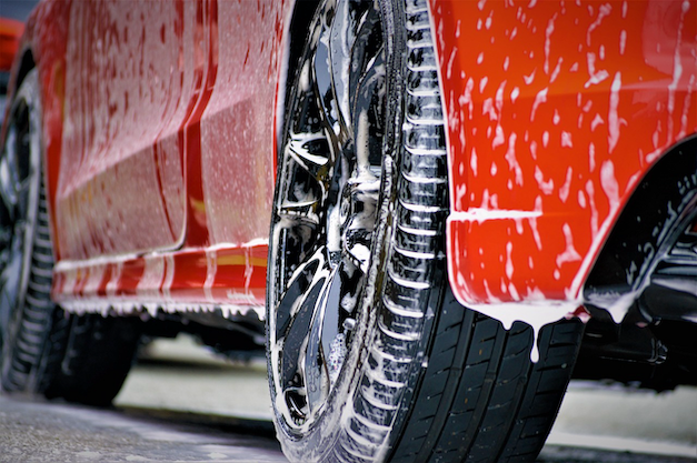 Close-up of a red car wheel covered in soap suds and water during a car wash in New Zealand.