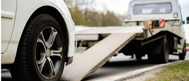 A close-up of a car tyre next to a flatbed tow truck ramp on the side of a New Zealand road.