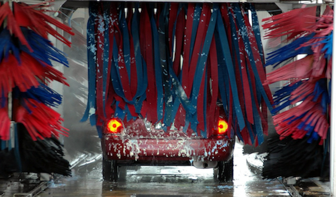 A car emerging from an automatic car wash with visible water spray, representing the car wash damage and insurance coverage guide that Quashed provides for New Zealand drivers in 2026.