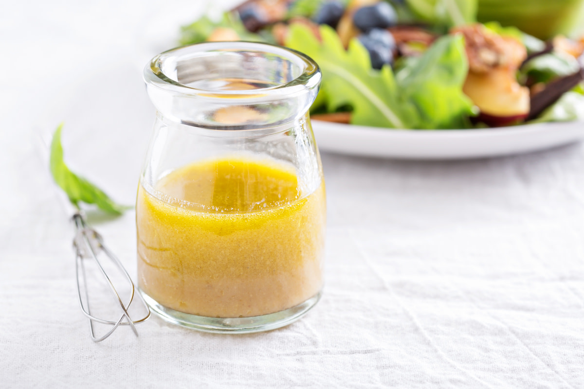 Vinaigrette in glass jar with salad in background and whisk