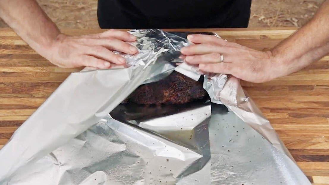 Aaron Franklin wrapping meat in tinfoil on wood