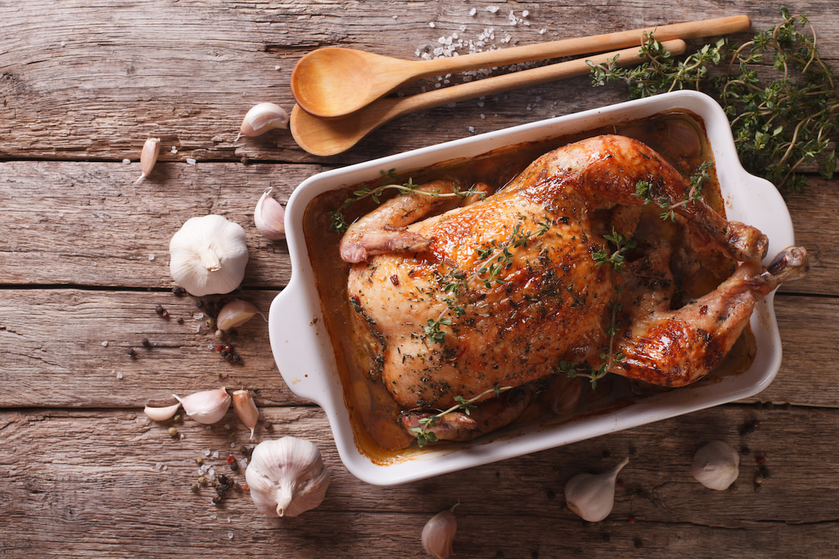 Roasted chicken in white dish with garlic and wooden spoons