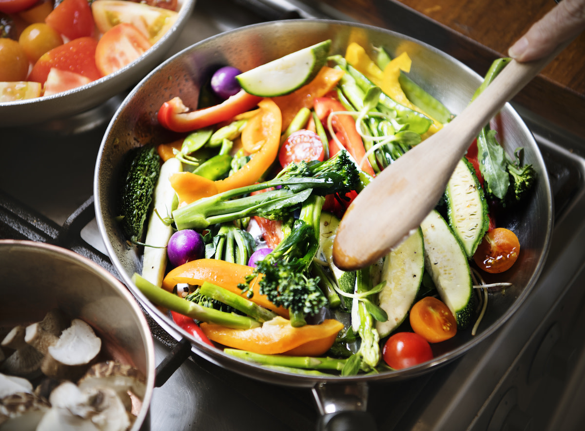 Vegetables being stir fried in pan with wooden spoon on stove