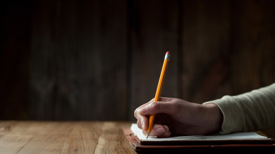 a person writing on paper with a pencil