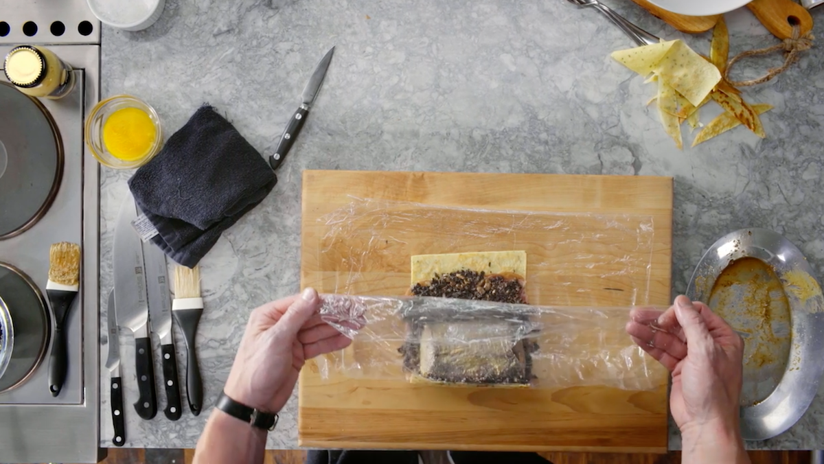 Plastic wrap being pulled over Beef Wellington