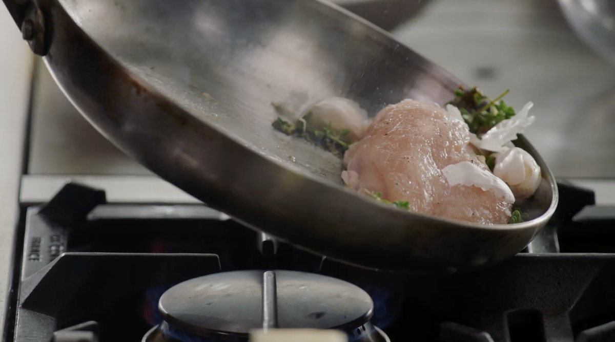 Chicken with garlic and herbs in pan being tilted