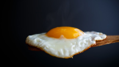 Fried egg on wooden spoon with black background