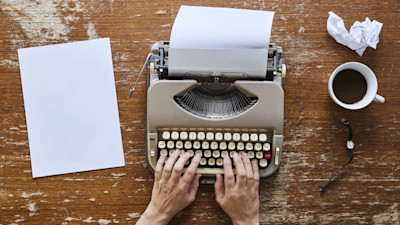 Hands on typewriter with coffee on wood