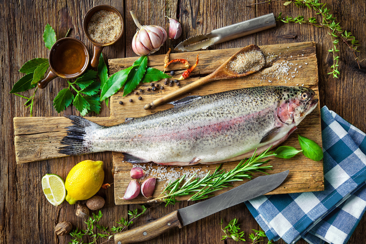 Raw trout on wood board with knife and ingredients