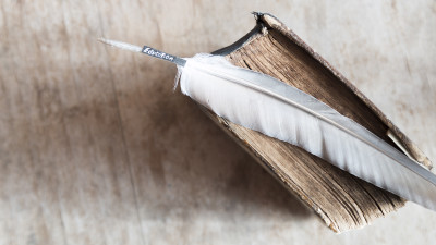 Old book with feather on white wood