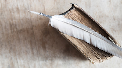 Old book with feather on white wood