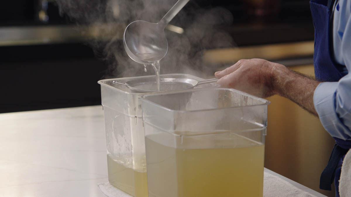 Thomas Keller straining chicken stock into plastic tubs