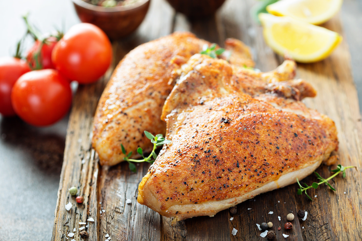 Baked chicken breast on wood with lemon and tomatoes