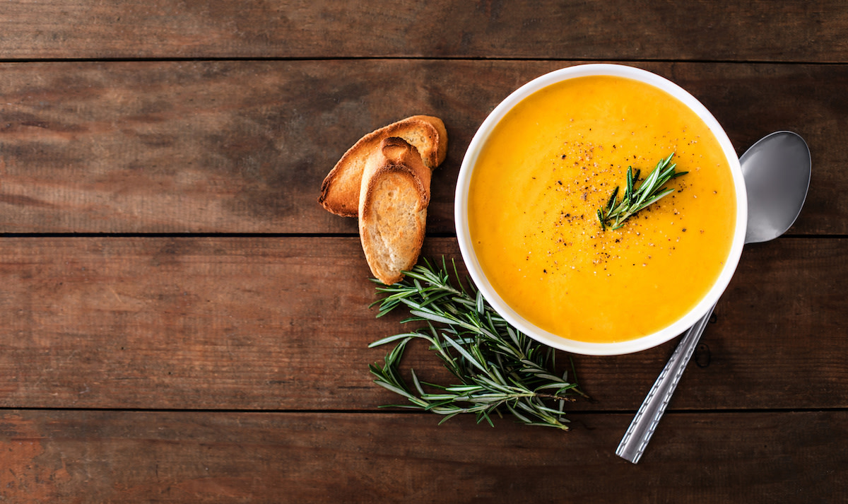 Butternut squash soup in white bowl with bread and rosemary