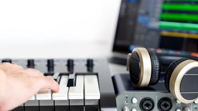 person playing electronic piano with headphones and recording gear