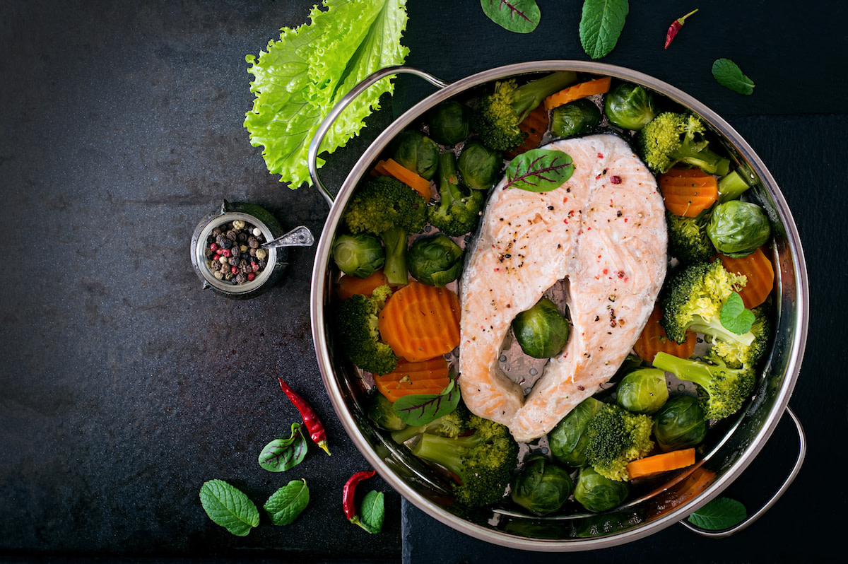 Vegetables and salmon in pot with water on black background