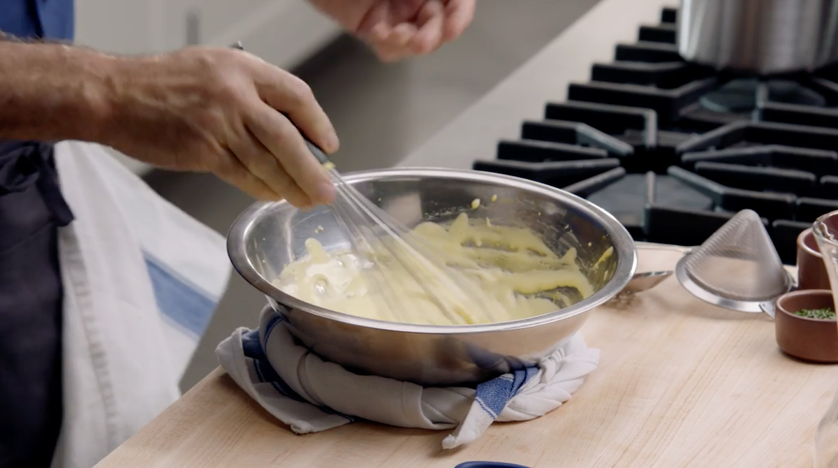 Thomas Keller whisking hollandaise sauce on cutting board