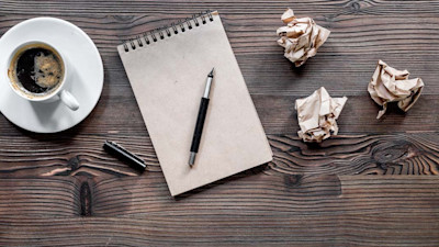 Notebook with coffee and crumpled up paper on wood