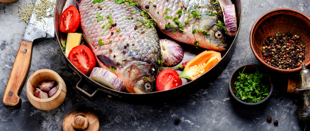 Raw carp fish in skillet with tomatoes onions and citrus