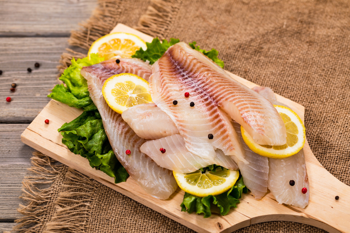 Raw tilapia filets with lettuce and lemon on wood board