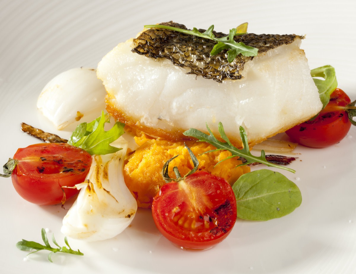 Cooked Chilean sea bass on plate with tomatoes onions and puree