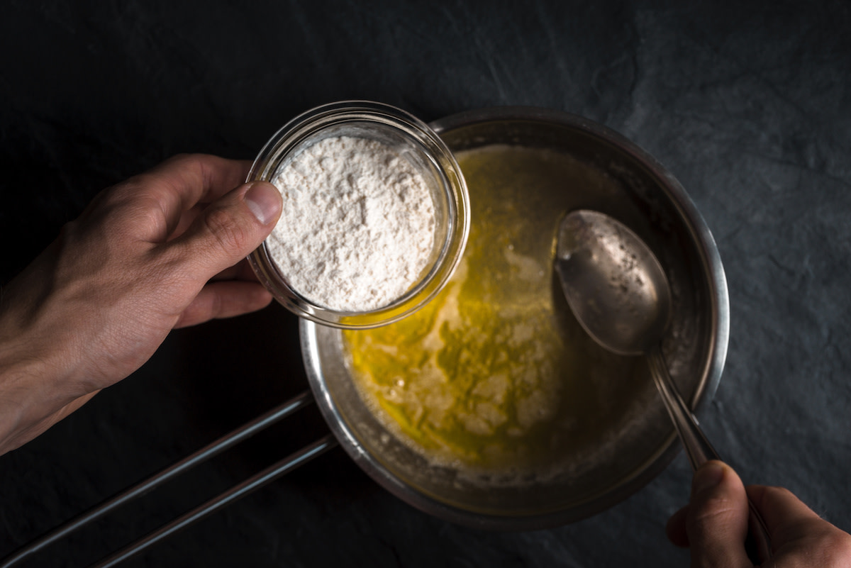 Person putting flour into melted butter in pot