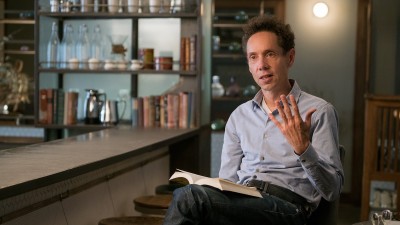Malcolm Gladwell sitting with book explaining something