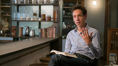 Malcolm Gladwell sitting with book explaining something