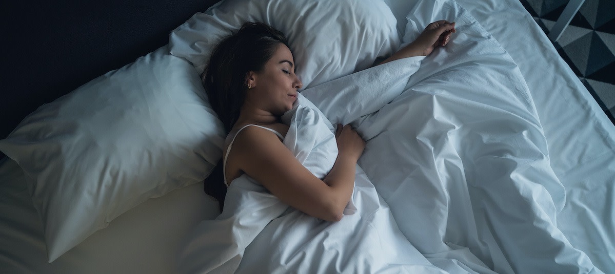  A young woman is sleeping in a bed and she is having trouble sleeping, which could be a symptom of a sleep disorder.