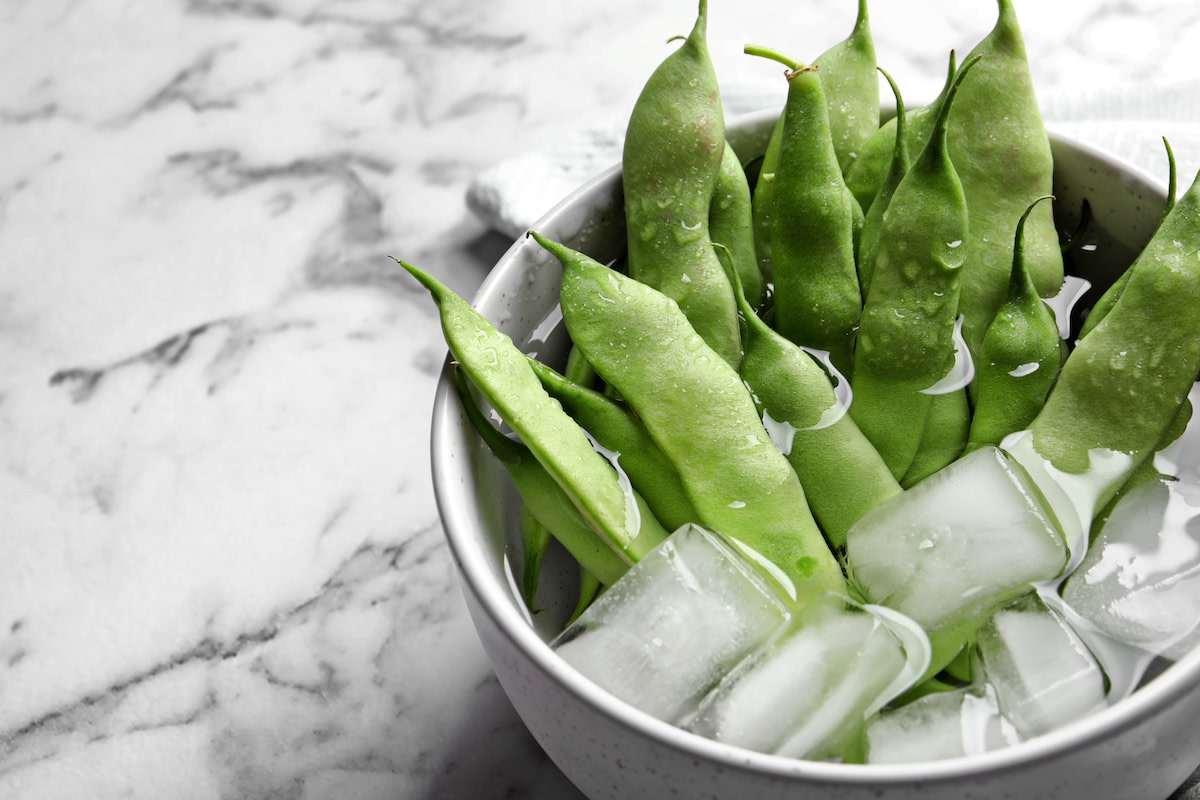 Snap peas in a bowl of ice water on marble