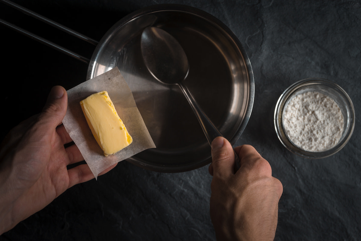 Person putting butter into pot with flour in bowl