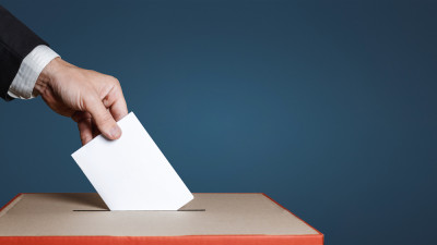 Man putting ballot into box with slot in it on blue background