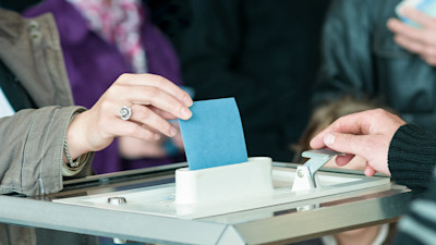 a person putting their ballot in the voting box