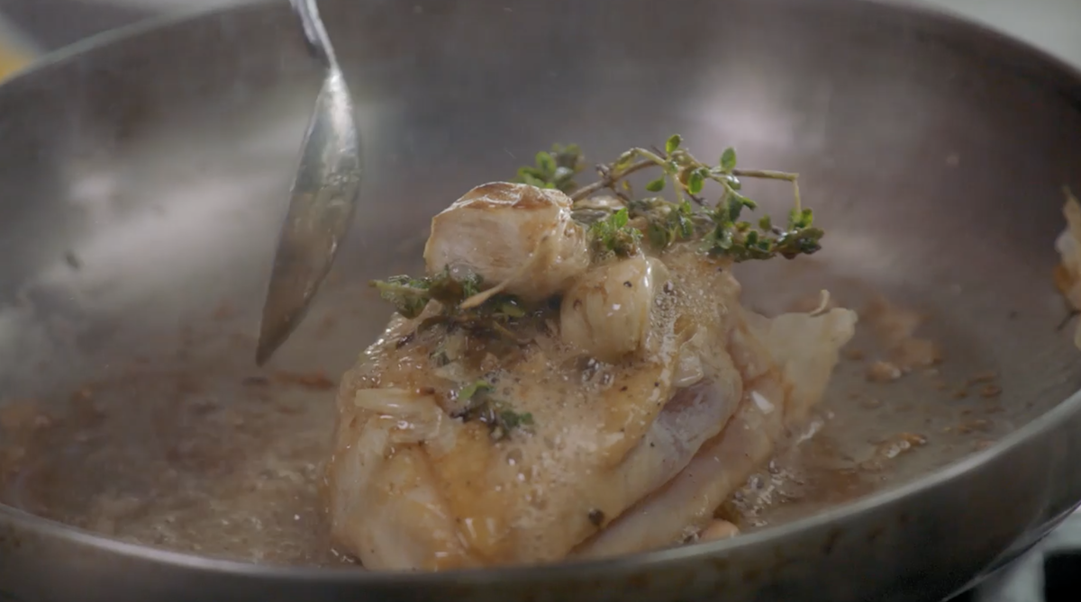 Chicken being cooked in pan with herbs and garlic