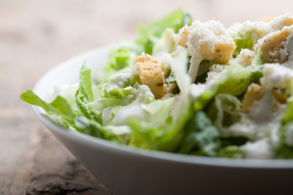 Caesar salad in white bowl with wood background