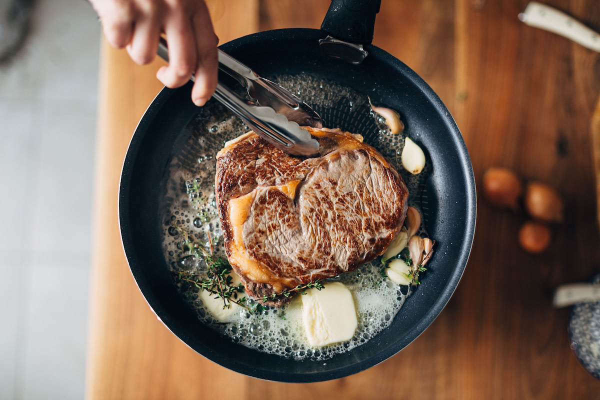 Steak in pan held by tongs with butter and garlic