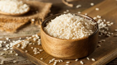 White uncooked rice in wooden bowl on wood plank