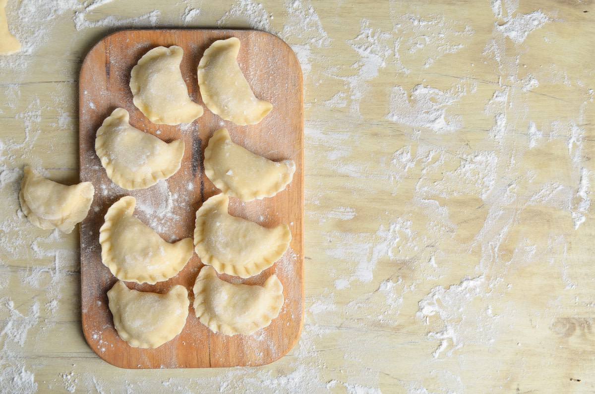 Raw pierogis on cutting board with flour