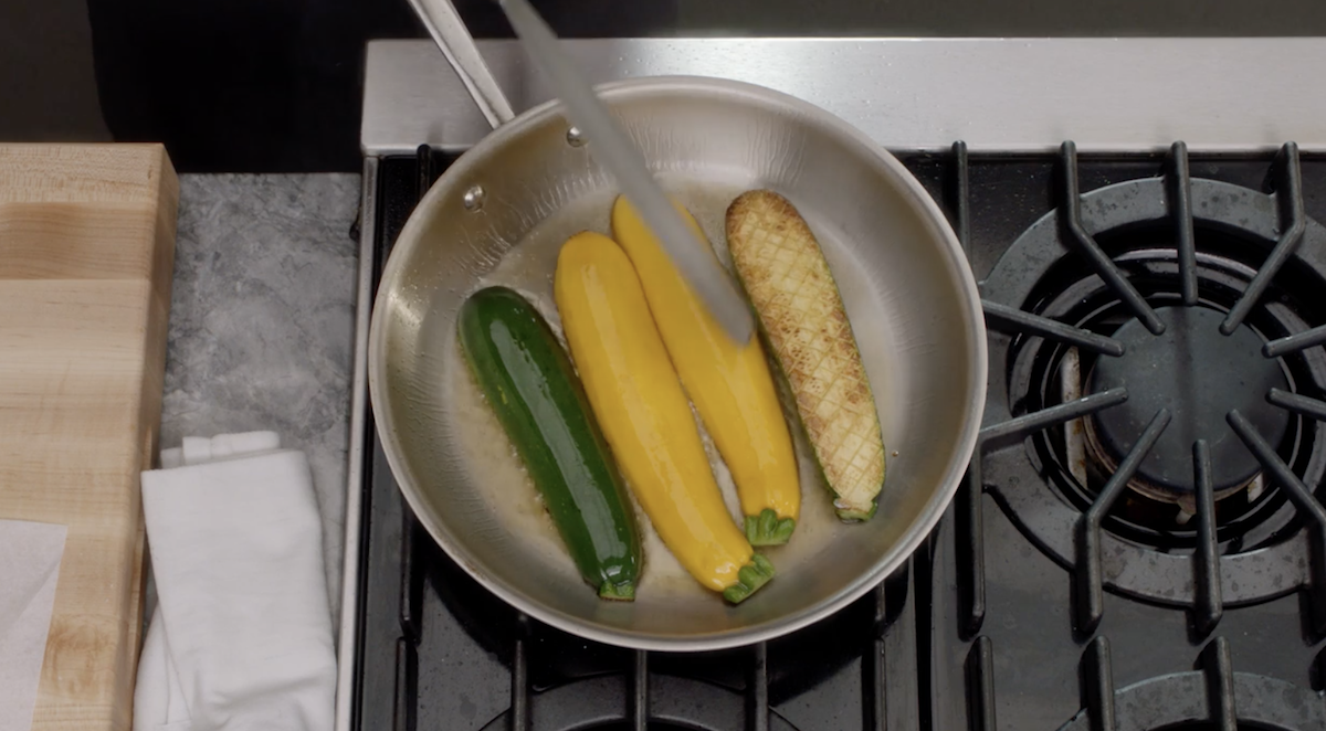 Zucchini on pan being flipped with tongs